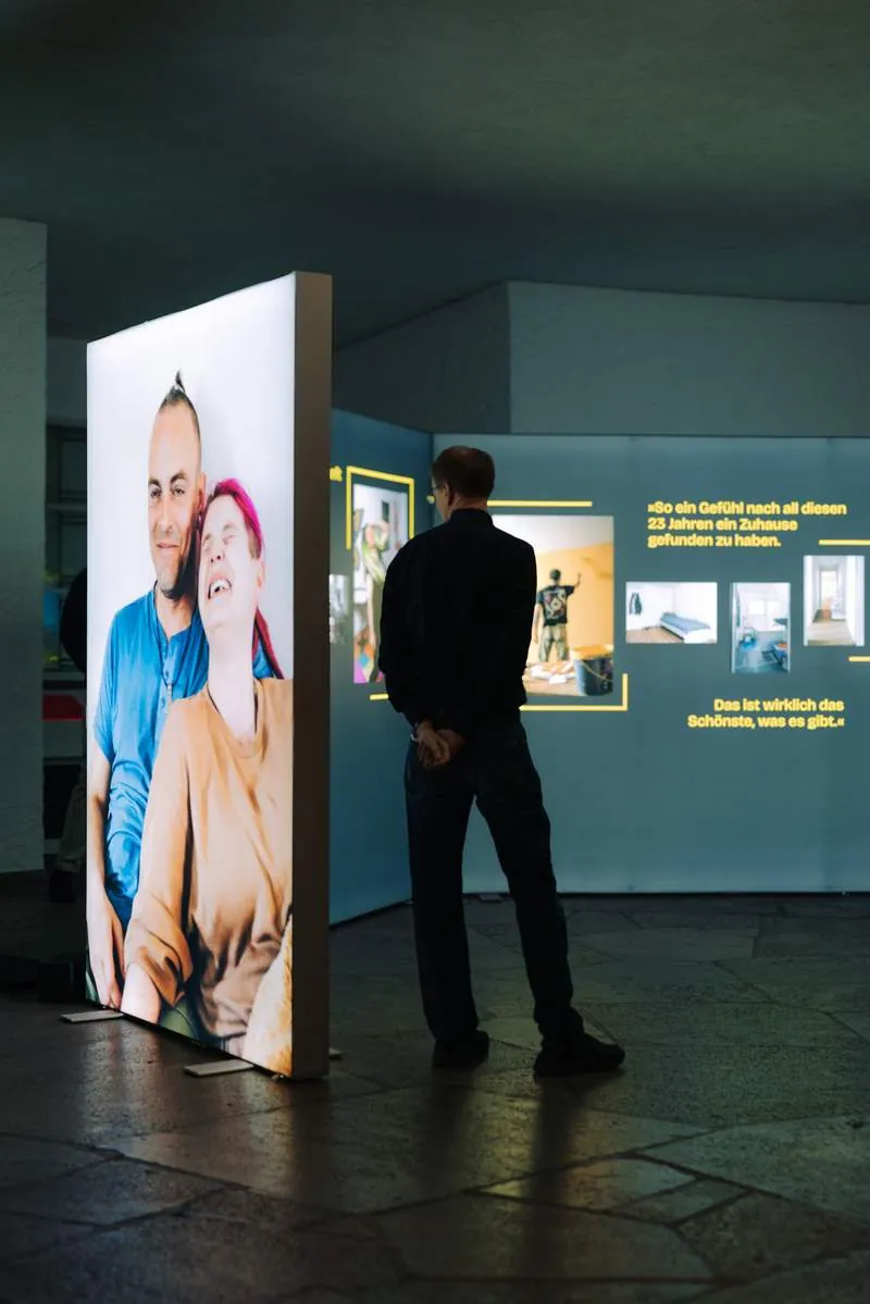 Leuchtkasten-Installation mit dem Porträt eines Paares, davor ein Besucher, HOME STREET HOME in der Frankfurter Paulskirche